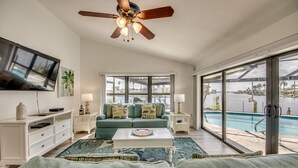A living room with a large TV, a ceiling fan, a sofa, a coffee table, and a view of a swimming pool. - Beautiful views, watch the dolphins and tarpon swim by on the  lanai or dock! (Cape Coral)