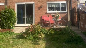 A two-story brick house with a tiled roof, a sliding glass door, and a small patio with a table and chairs. - Stunning 3 -bed Semi Detached House in Cambridge (Cambridge)