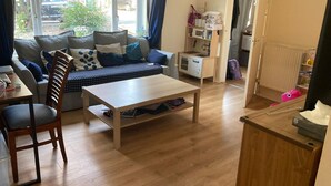 A living room with a sofa, a wooden table, and a small kitchenette area. - Stunning 3 -bed Semi Detached House in Cambridge (Cambridge)