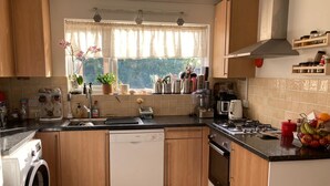 A kitchen with wooden cabinets, a dishwasher, a stove, and a window with a view of greenery. - Stunning 3 -bed Semi Detached House in Cambridge (Cambridge)