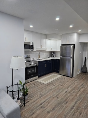 A modern kitchen with white cabinets, stainless steel appliances, and a wooden floor.