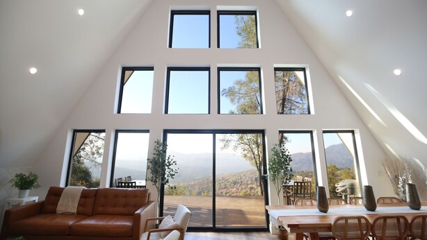 A spacious loft with a high ceiling, large windows offering mountain views, a cozy seating area, and a dining space. - High End A-Frame - Hot tub - Awesome Views - Yosemite - Bass Lake - EV Charger (Oakhurst)
