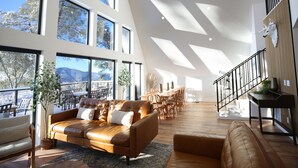 A spacious living area with a large window, a leather sofa, and a dining area with wooden furniture. - High End A-Frame - Hot tub - Awesome Views - Yosemite - Bass Lake - EV Charger (Oakhurst)