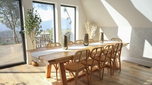 A dining area with a wooden table and chairs, large windows with a view of the outdoors, and a decorative vase on the table. - High End A-Frame - Hot tub - Awesome Views - Yosemite - Bass Lake - EV Charger (Oakhurst)