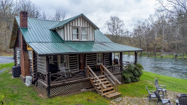 A log cabin with a green metal roof, a porch with steps, and a view of a river. - Brown Trout (Bristol)
