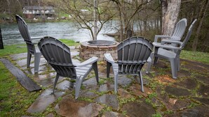 A stone patio with Adirondack chairs around a stone fire pit, overlooking a river. - Brown Trout (Bristol)