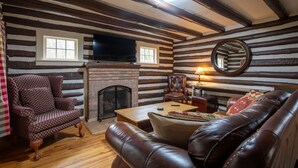 A log cabin interior with a fireplace, leather furniture, and a television mounted on the wall. - Brown Trout (Bristol)