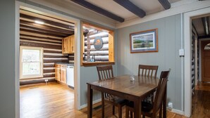 A dining area with a wooden table and chairs, a kitchen with wooden cabinets, and a log wall with a window. - Brown Trout (Bristol)