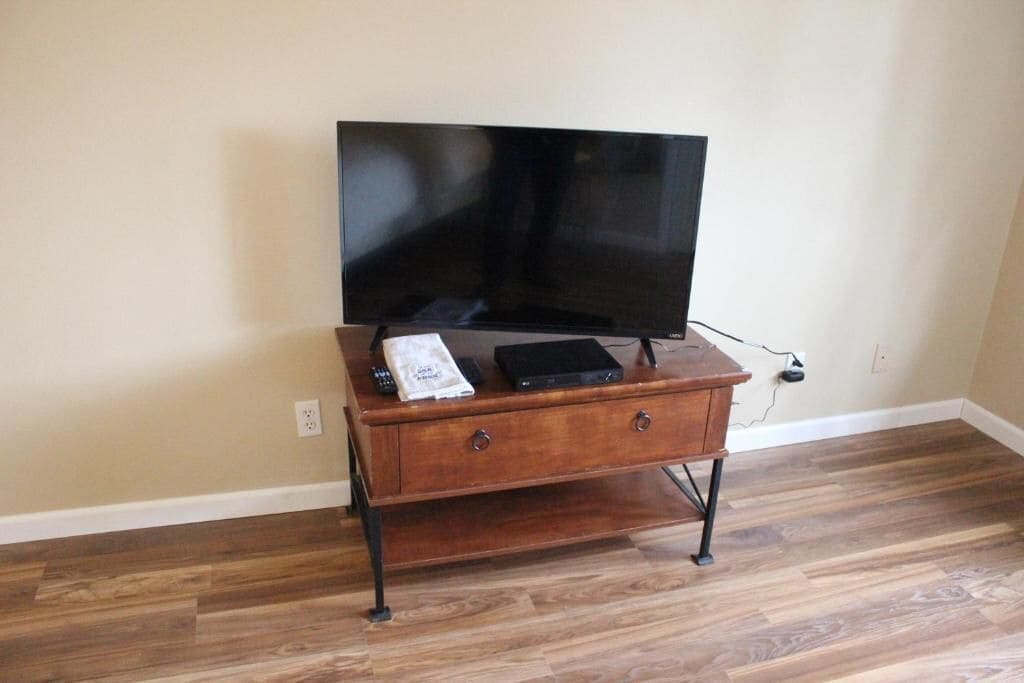 A wooden TV stand with a flat-screen TV, a remote, and a power strip.