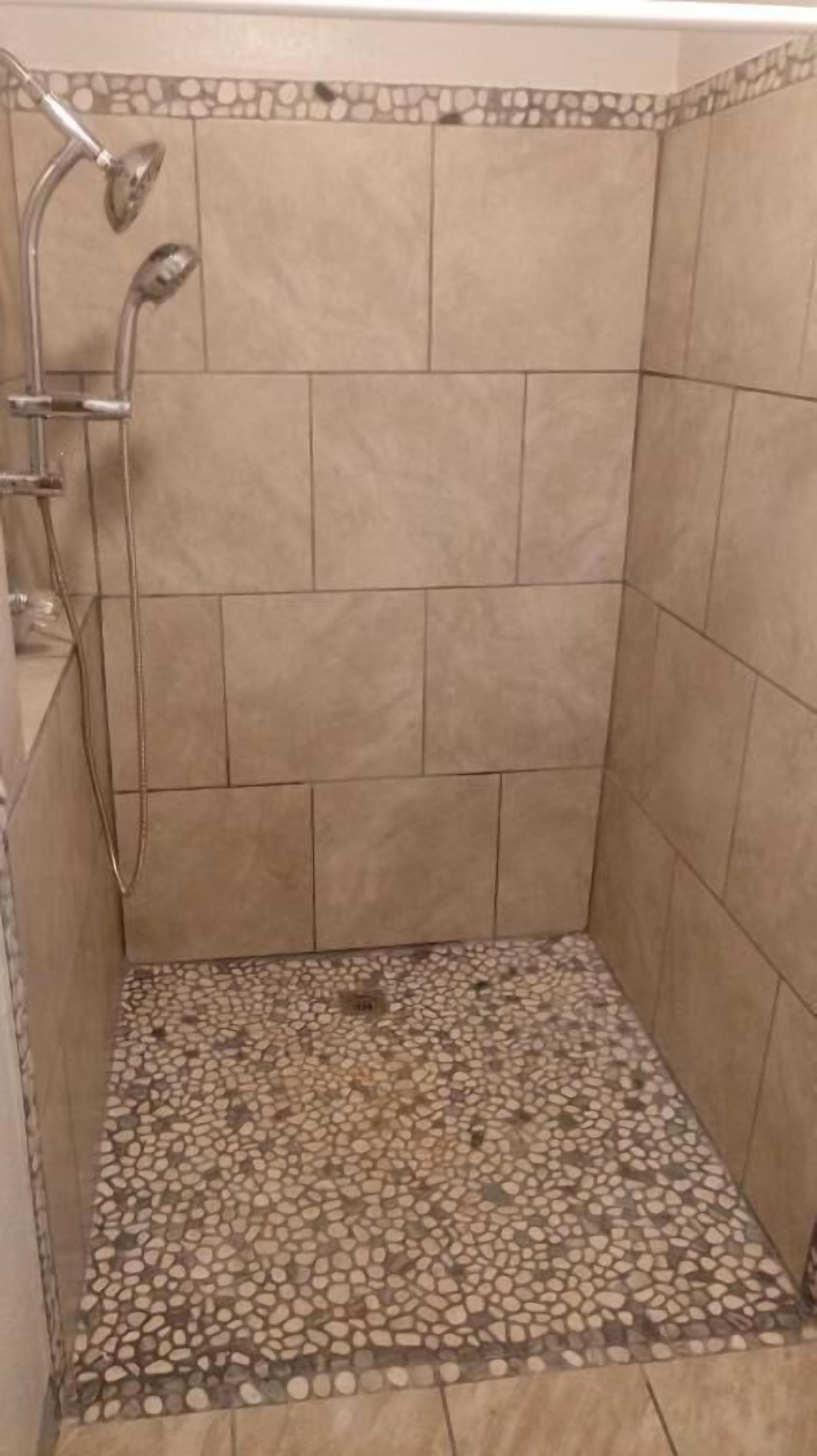 Een douche met een vloer van kiezeltegels en een stenen rand.