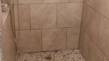 Een douche met een vloer van kiezeltegels en een stenen rand.