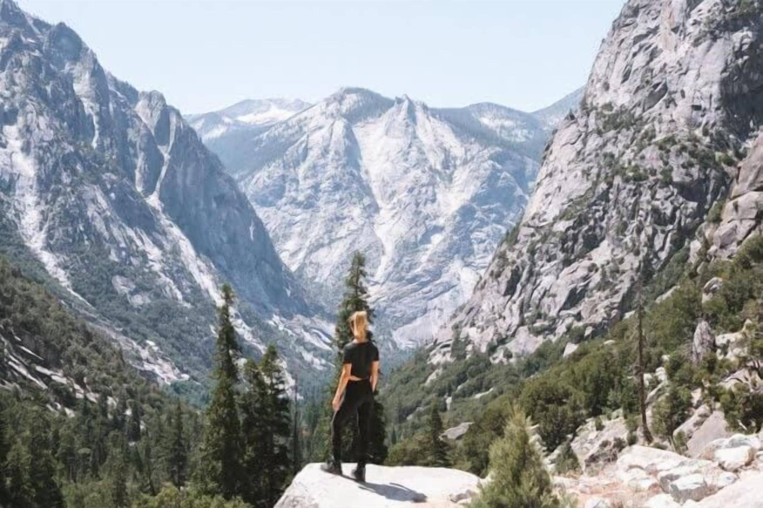 A person standing on a rock in a mountainous area with rocky terrain and trees.