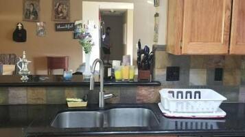 A kitchen with wooden cabinets, a black countertop, a stainless steel sink, and a dishwasher.