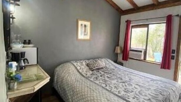 Un dormitorio con cama, escritorio con lámpara, ventana con cortinas y techo con vigas de madera.