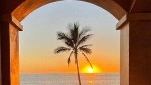 Un balcón con vista al atardecer sobre el océano, enmarcado por un arco de madera.