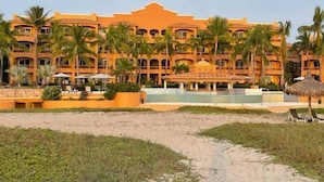 Un resort con múltiples balcones, palmeras, una piscina y una zona de playa.