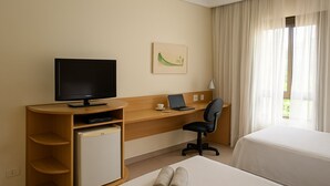 A hotel room with a bed, a desk with a computer, a television, and a small refrigerator. - Elegance Suites Franca (Franca)