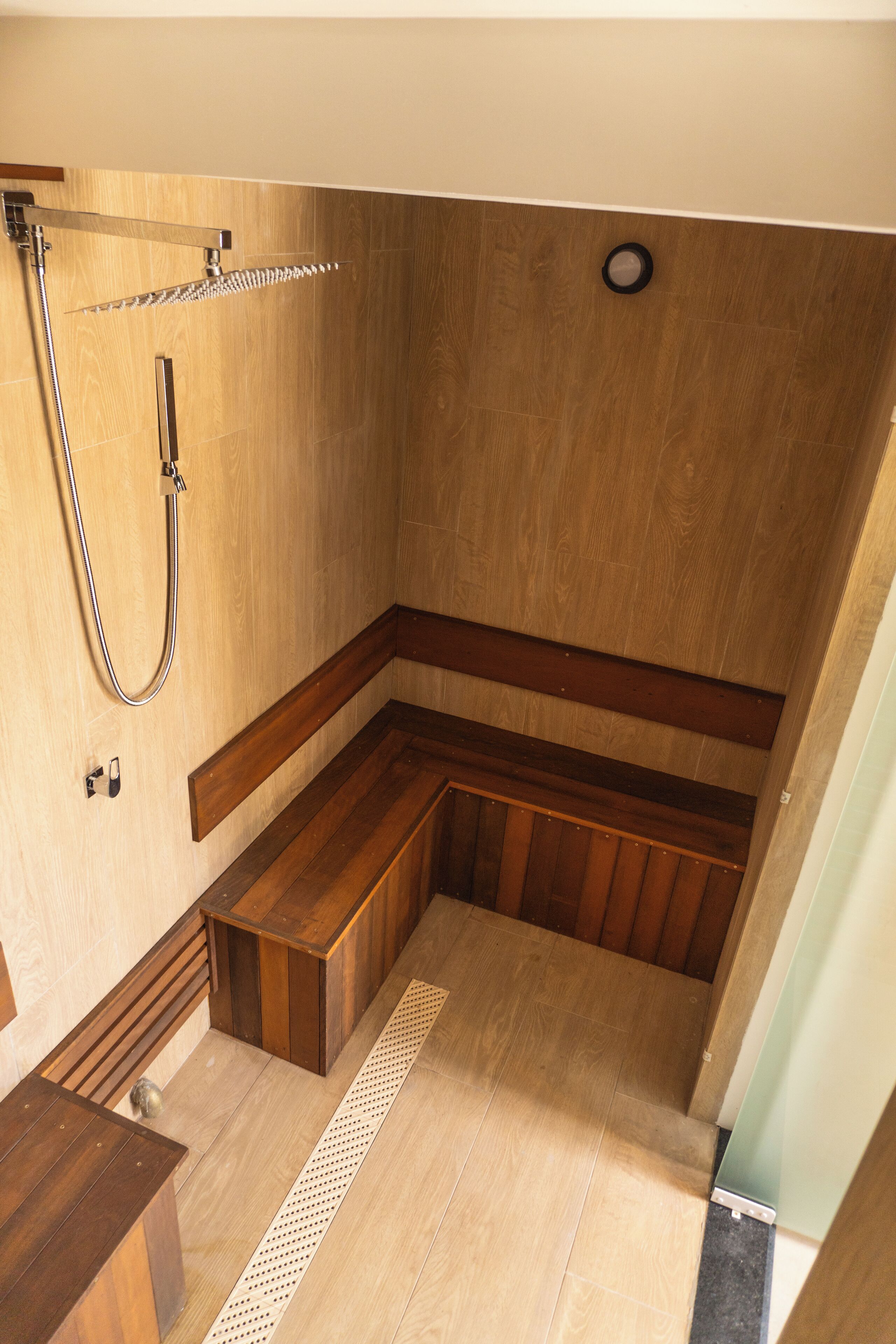 A wooden shower enclosure with a built-in bench, a handheld showerhead, and a wall-mounted control.