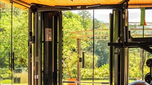 A gym with exercise equipment, a bench, and a view of greenery. - Village du Lac Hotel (Pomerode)