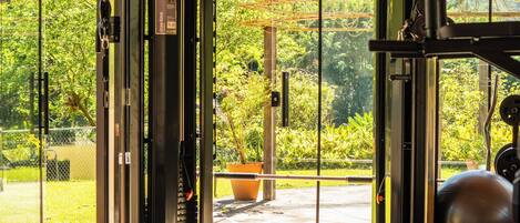 Une salle de sport équipée de matériel d’exercice, avec un banc et une vue sur la verdure.