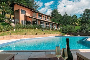 A modern house with a swimming pool, surrounded by lush greenery and a clear blue sky. - Village du Lac Hotel (Pomerode)