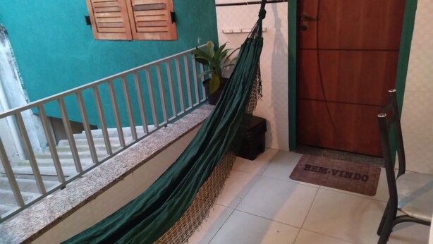 A room with a green hammock, a wooden door, and a white wall with a window. - Rua Anápolis (Guarulhos)
