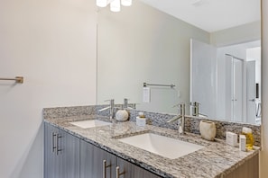 A modern bathroom with two sinks, a large mirror, and a granite countertop.
