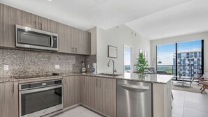 A modern kitchen with a built-in microwave, oven, and dishwasher, granite countertops, and a large window offering a view of the city.