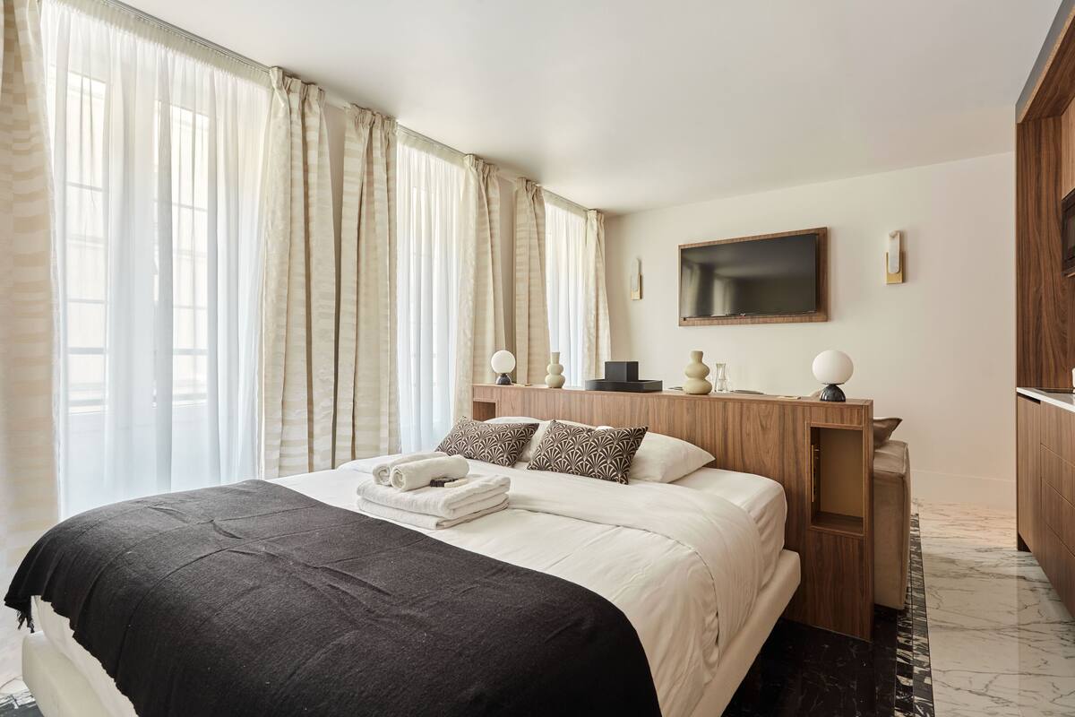 A hotel room with a large bed, a wooden headboard, a flat-screen TV, and a marble floor.
