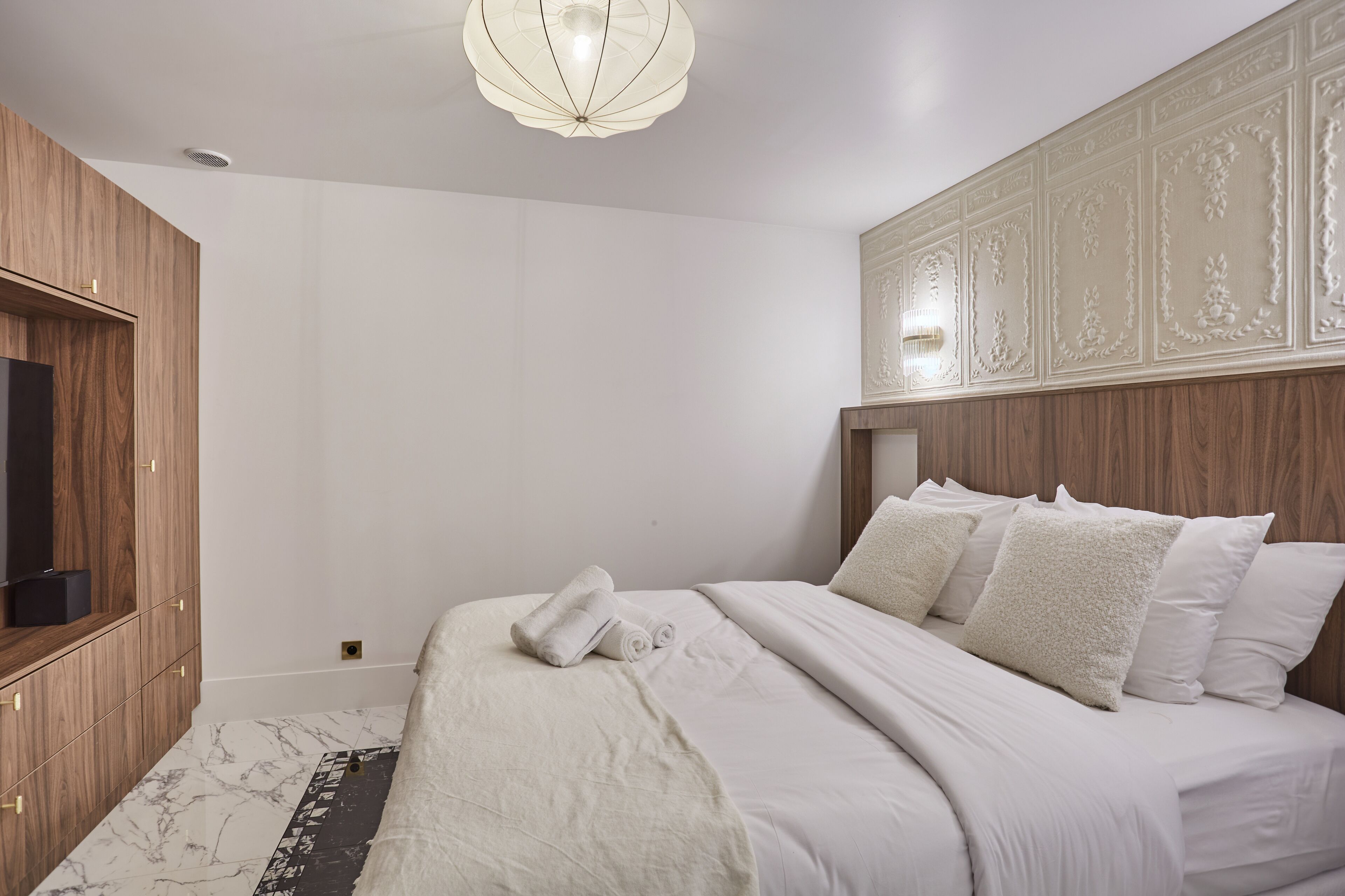 Un dormitorio con una cama, un armario de madera y una lámpara decorativa en el techo.