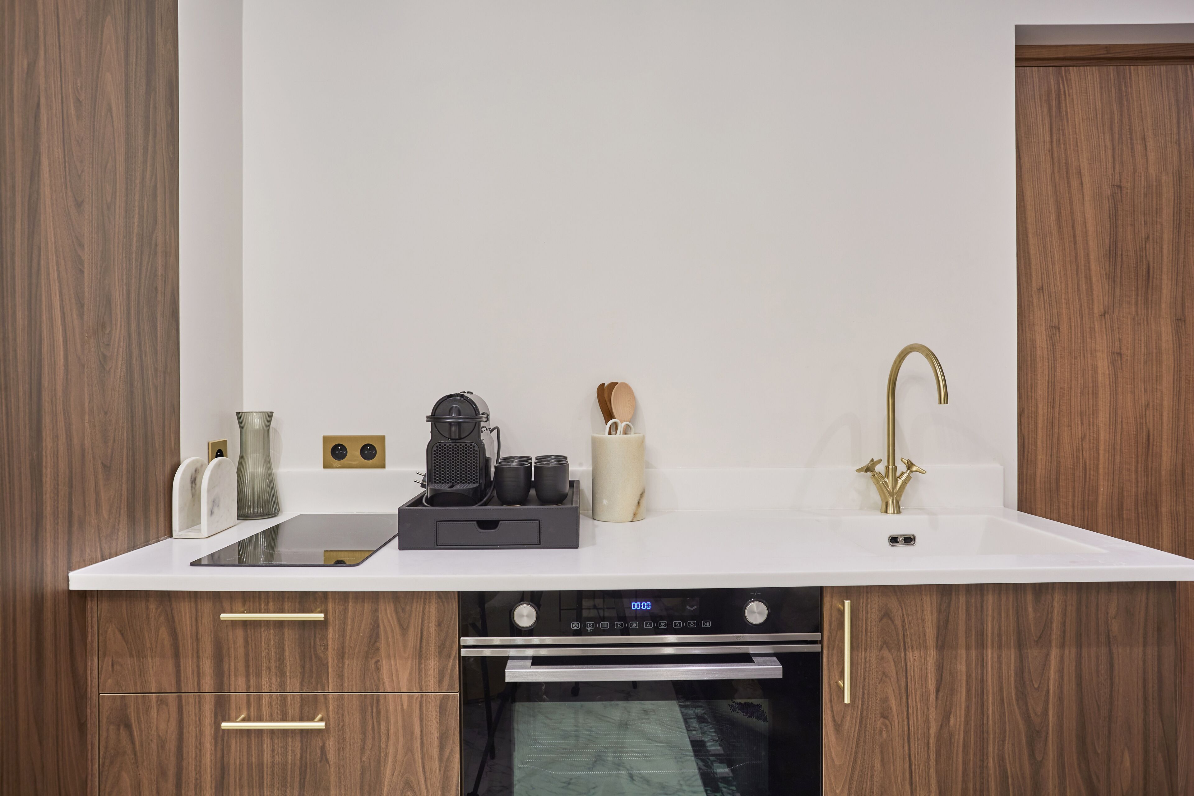A modern kitchen with wooden cabinets, a white countertop, a built-in oven, and a stainless steel faucet.
