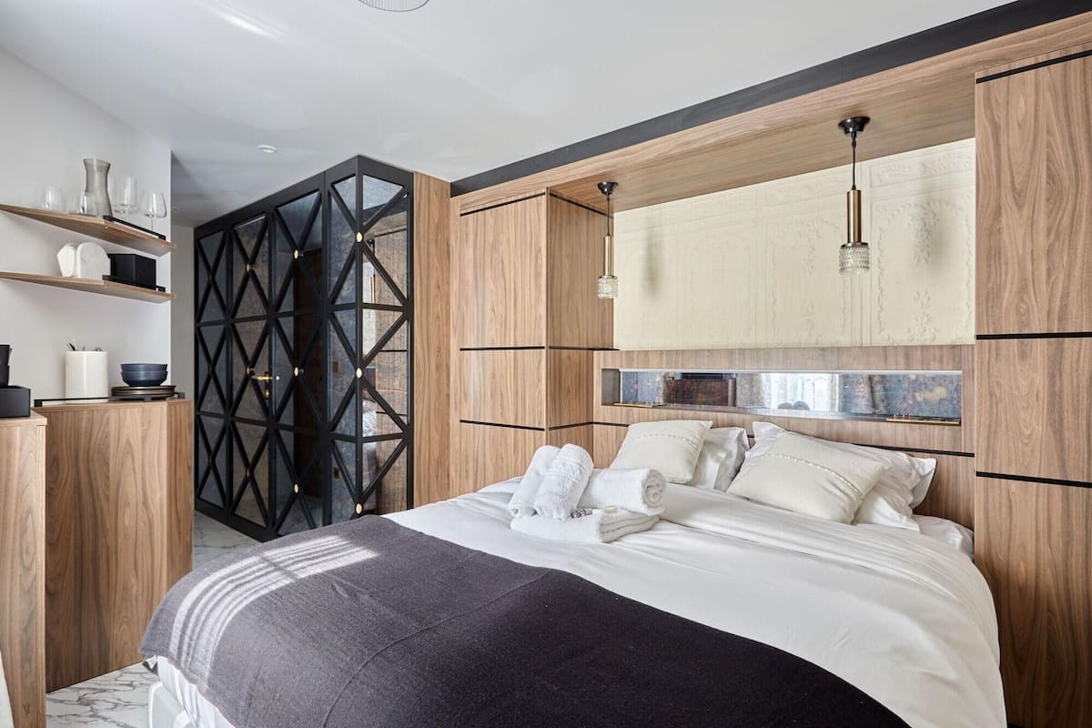 A modern bedroom with a bed, wooden headboard, and a geometric wall design.