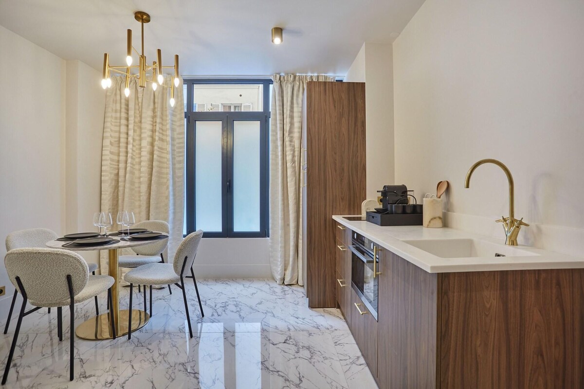 A modern kitchen with a marble countertop, a gold faucet, and a dining area with a table set for two.