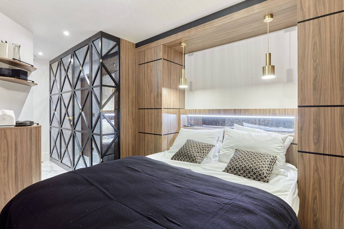A modern bedroom with a wooden headboard, a geometric partition, and a bed with patterned pillows.