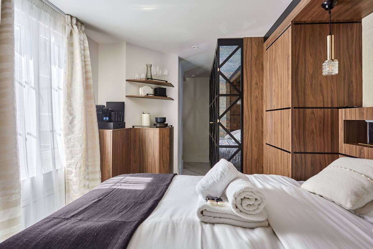 A modern hotel room with a neatly made bed, wooden wardrobe, and a coffee machine on a wooden cabinet.