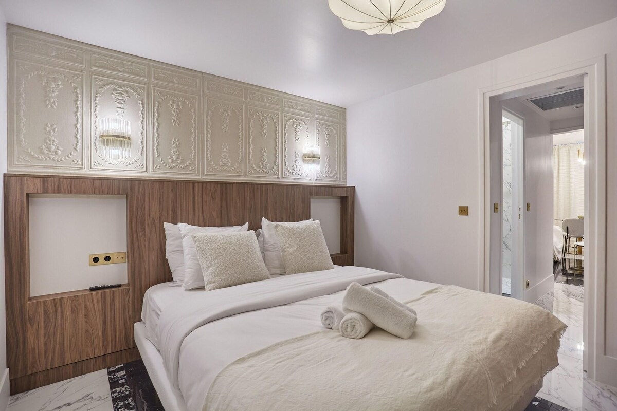 A hotel room with a large bed, a wooden headboard, and a wall-mounted light fixture.