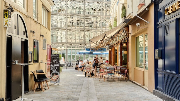 Una calle estrecha con mesas al aire libre, un café y un escaparate azul.