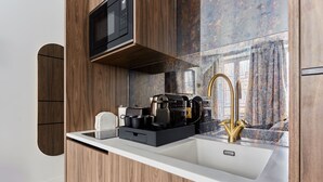 Cocina moderna con armarios de madera, encimera blanca, pileta de acero inoxidable, grifo dorado y microondas negro.
