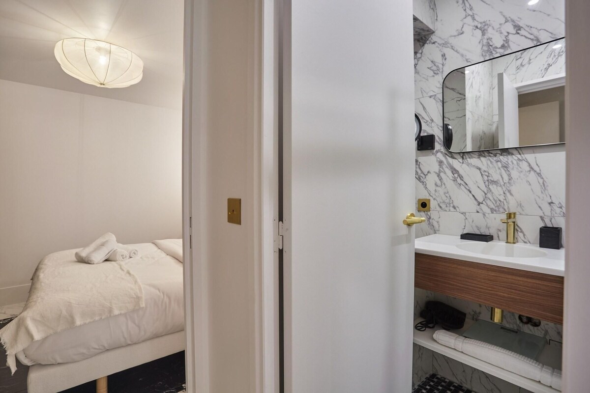 A hotel room with a bed, a bathroom with a marble wall, a sink, and a mirror.