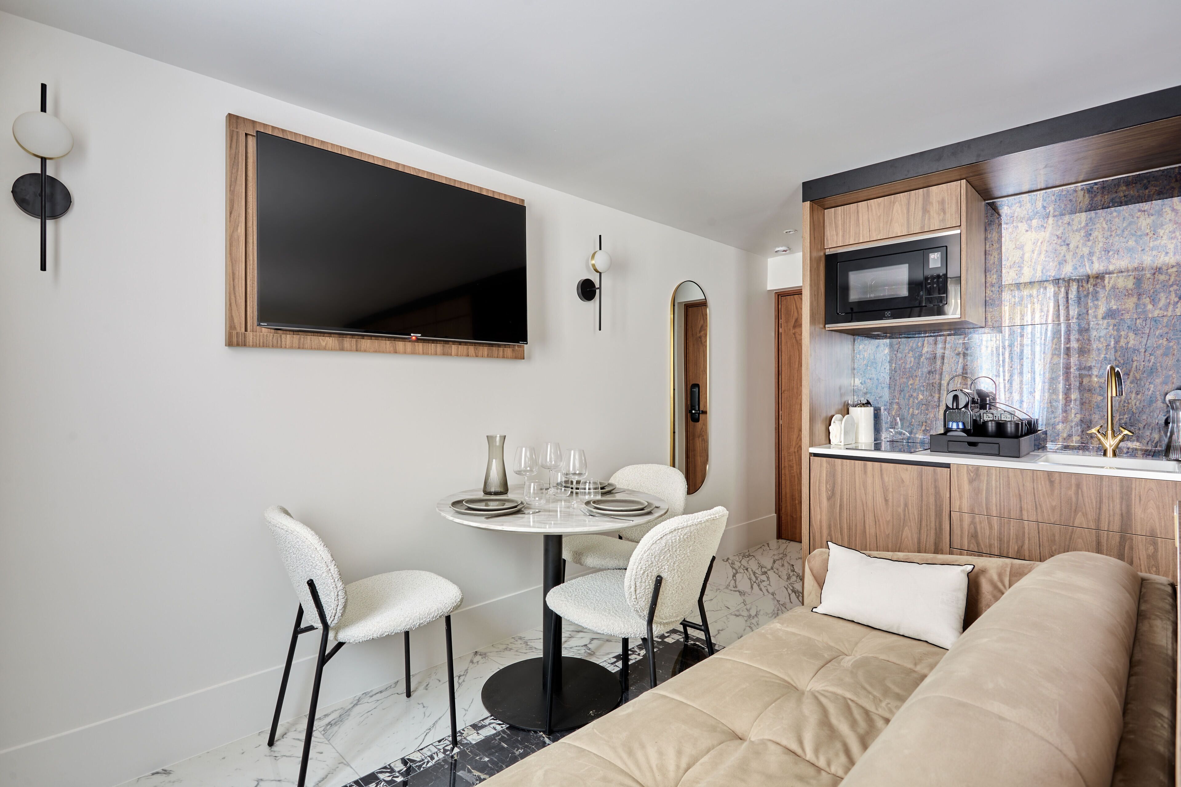 A compact living space with a dining area, a sofa, a kitchen with a microwave, and a large mirror.