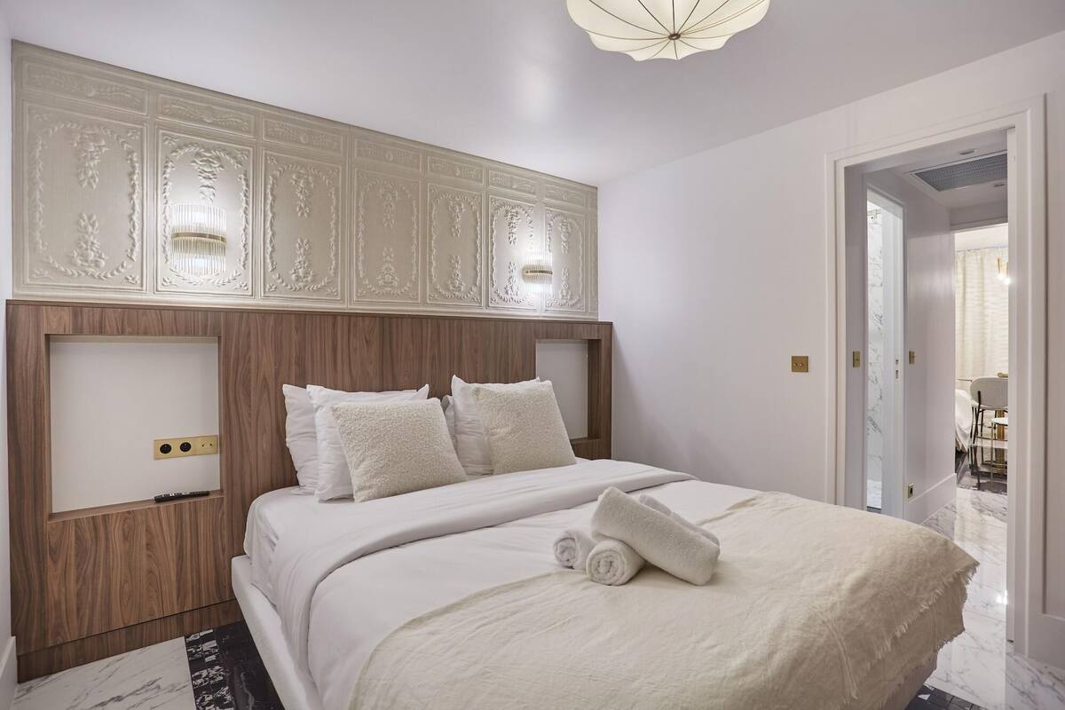 A bedroom with a wooden headboard, white bedding, and a ceiling light fixture.
