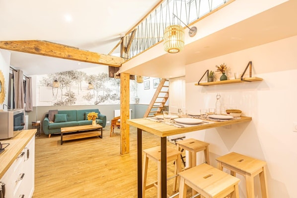 A cozy living area with a wooden dining table set for four, a green sofa, and a staircase leading to an upper level.