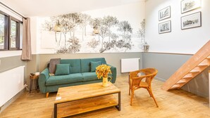 A living room with a green sofa, a wooden coffee table, a wicker chair, and a wall with framed pictures. - Charming apartment in Gentilly-  door of Paris (Gentilly)