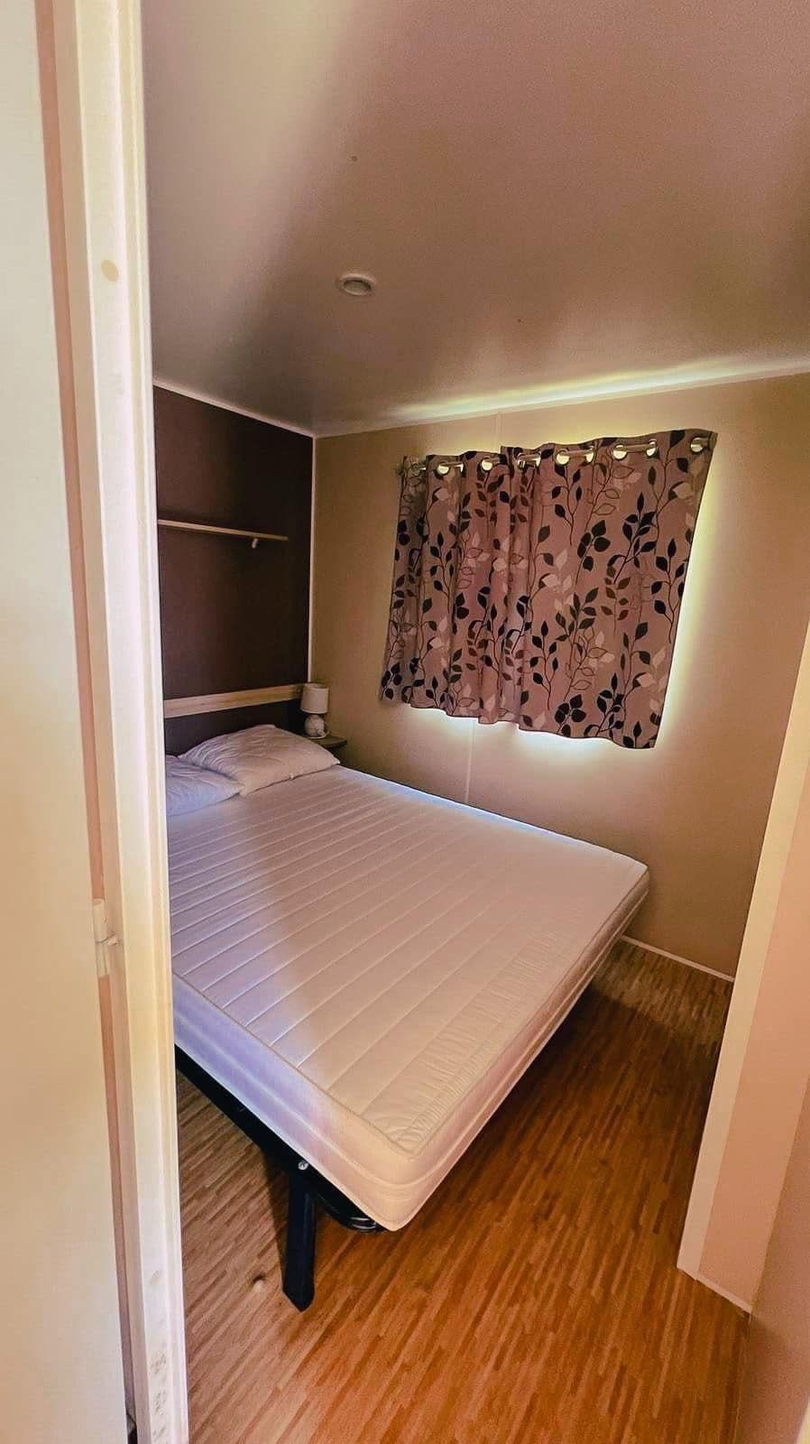 Ein kleines Zimmer mit einem Einzelbett, Holzboden, einem Fenster mit blumigem Vorhang und einem eingebauten Kleiderschrank.