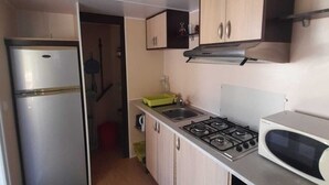 A compact kitchen with a refrigerator, stove, microwave, and wooden cabinets. - Spacious chalet with furnished terrace (Fréjus)