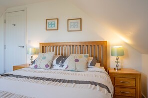A bedroom with a wooden headboard, two bedside tables with lamps, a bed with patterned bedding, and two framed pictures on the wall. - The Sheiling - Three Bedroom House, Sleeps 6 (Woolacombe)