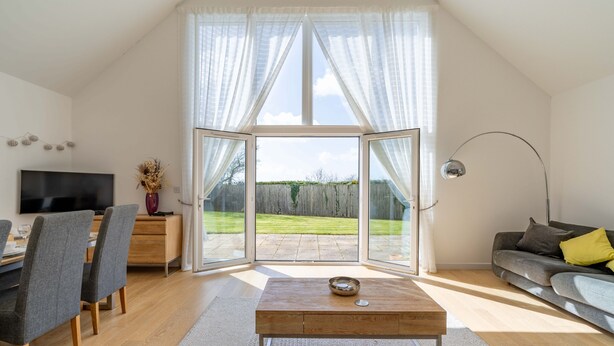 A modern living room with a TV, dining area, and a large sliding glass door leading to a backyard. - The Sheiling - Three Bedroom House, Sleeps 6 (Woolacombe)