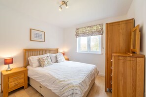 A bedroom with a bed, bedside table, lamp, wardrobe, window with curtains, and a ceiling light fixture.