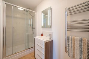 A bathroom with a glass-enclosed shower, a white sink with a mirror above it, and a towel rack with a striped towel. - The Sheiling - Three Bedroom House, Sleeps 6 (Woolacombe)