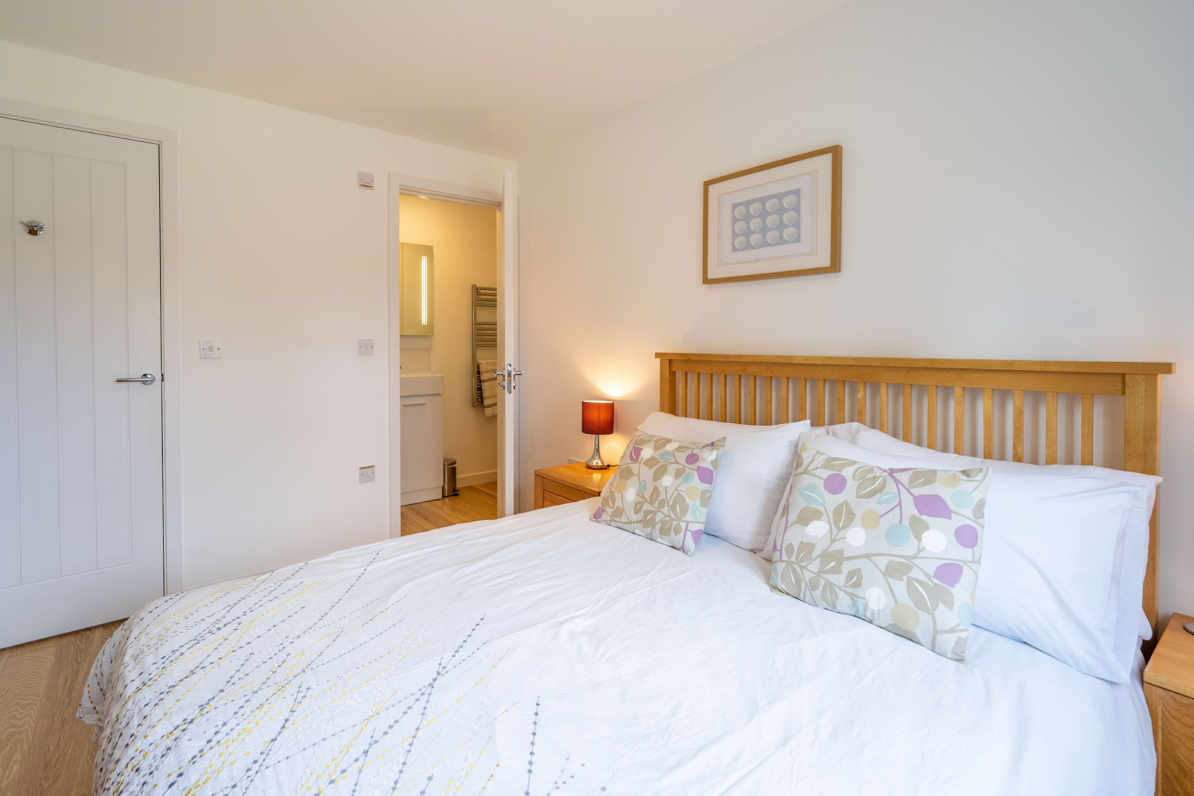 Un dormitorio con cama, mesita de noche, lámpara de noche y una puerta a otra habitación.